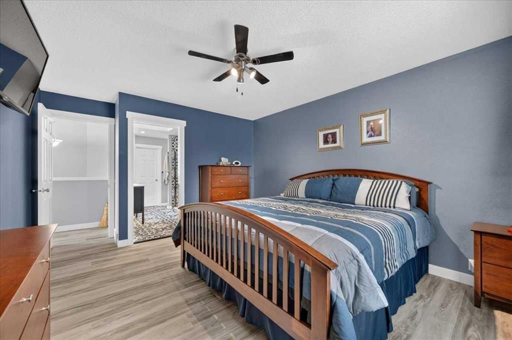 Bedroom with a wooden bed, blue walls, ceiling fan, and dresser on a light wood floor.