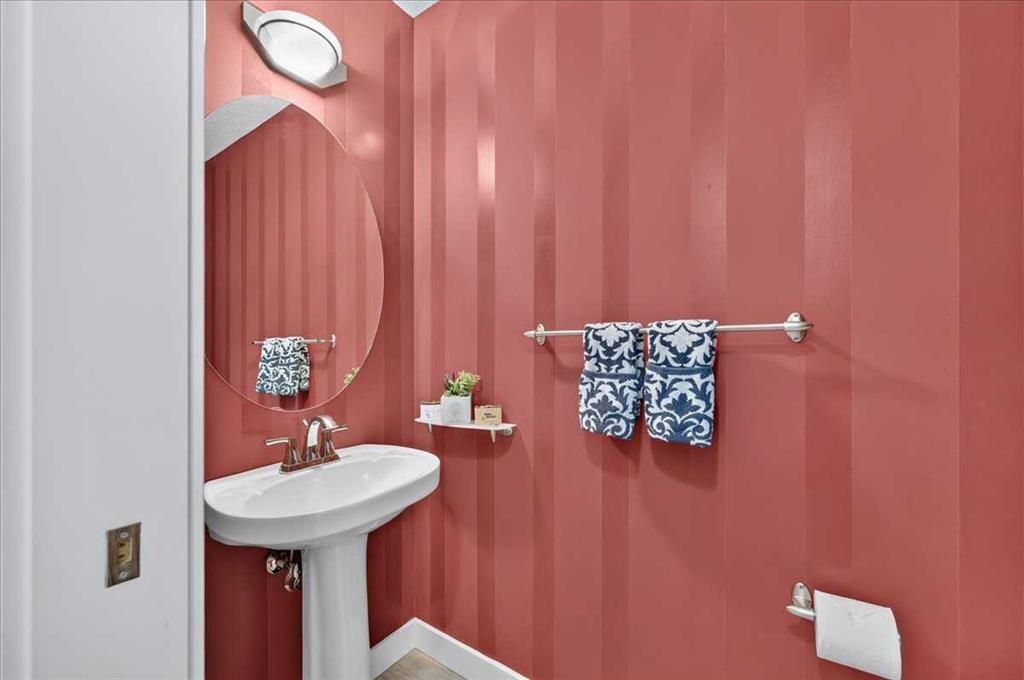 Small bathroom with pink striped walls, pedestal sink, oval mirror, and towel bar with blue towels.