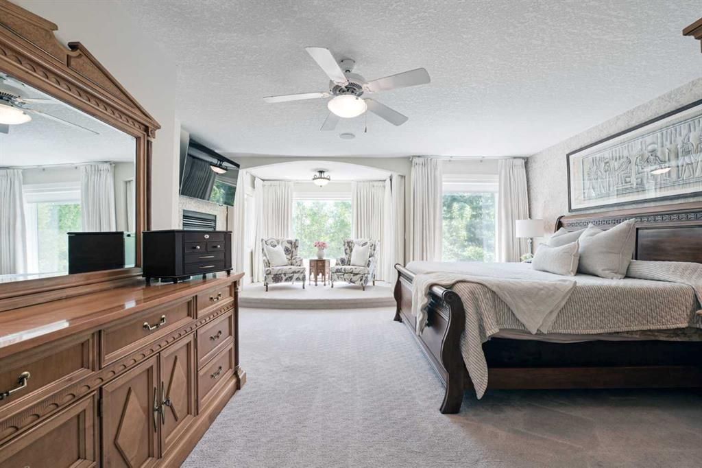 Bright bedroom with a bed, dresser, ceiling fan, and large windows overlooking a balcony