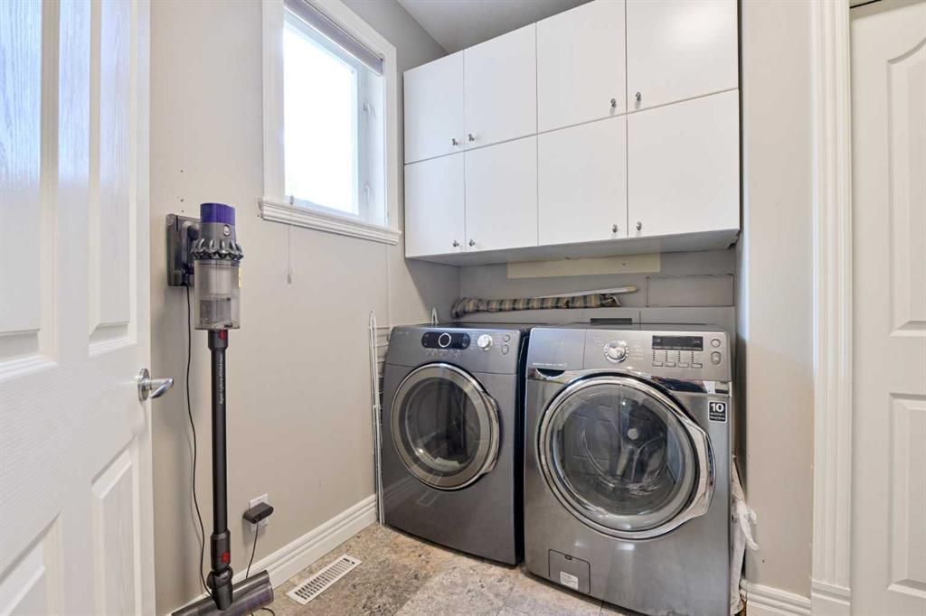 Laundry room with front-loading washer and dryer, white cabinets, and a small window.