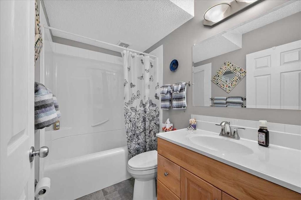 Bathroom with white tub, shower curtain, toilet, and wood vanity with a large mirror.