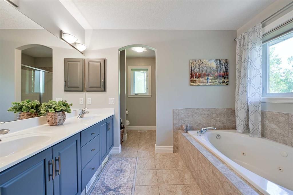 Bright modern bathroom with blue vanity, double sinks, large mirror, and a tiled tub by a window.