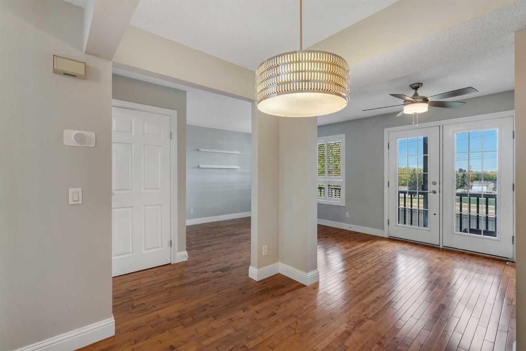 Bright empty dining room with hardwood floors, chandelier, and French doors to a balcony