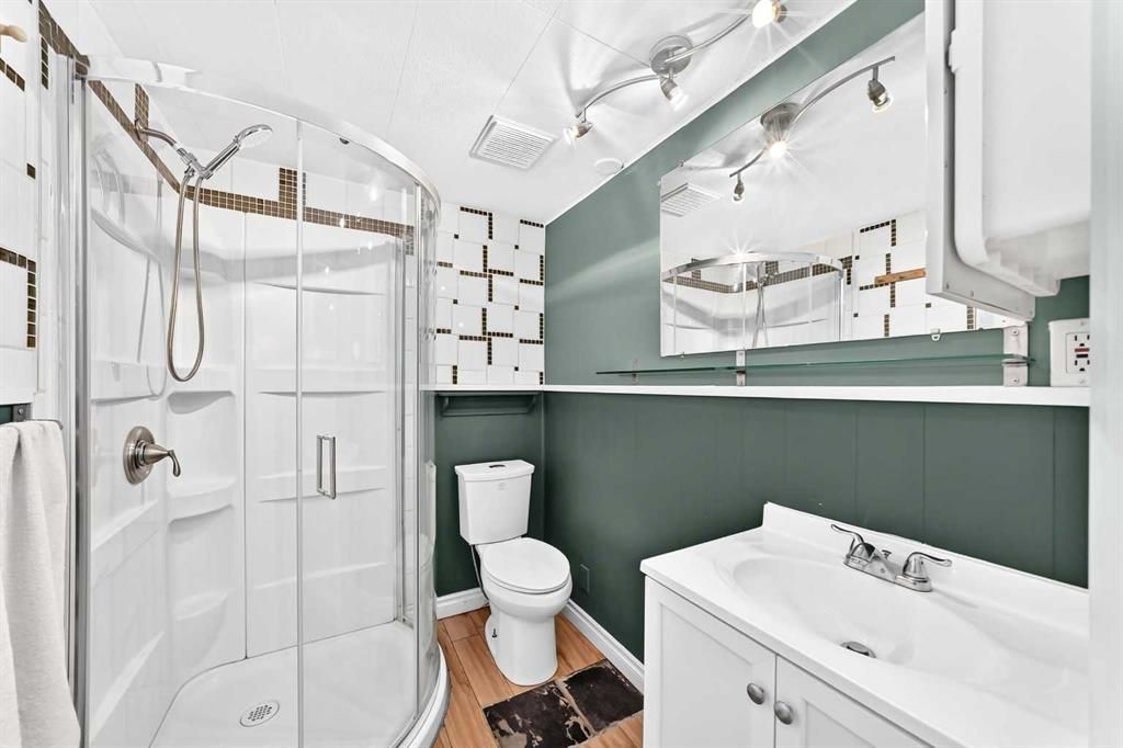 Compact white bathroom with shower, toilet, sink, and green accent wall under bright lighting