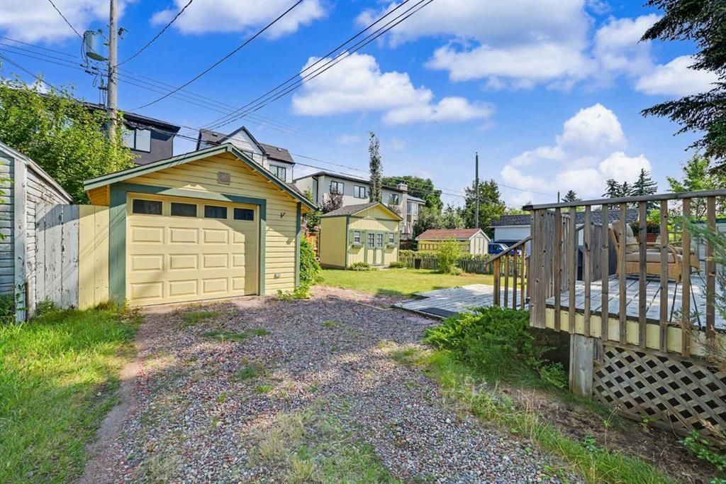 Gravel driveway beside a yellow garage and wooden fence under a blue sky with clouds