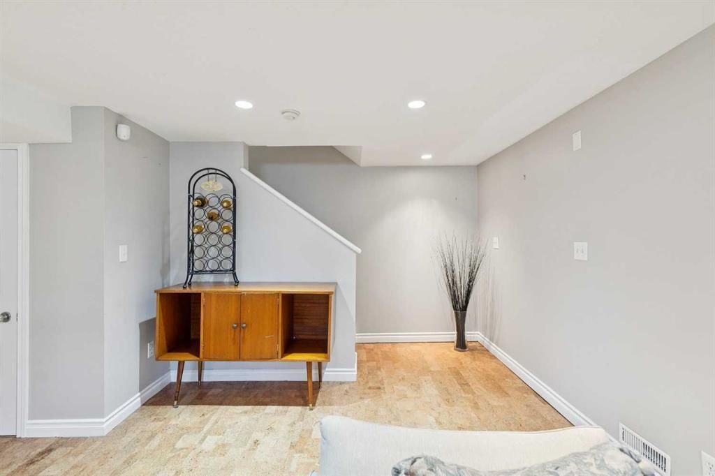 Bright minimalist living room with a wooden sideboard, staircase, and decorative vase on a light wood floor.