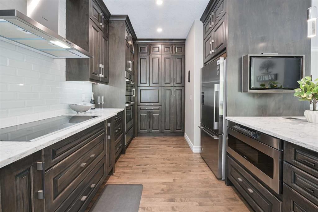 Modern kitchen with dark wood cabinets, white countertops, stainless appliances, and light wood flooring