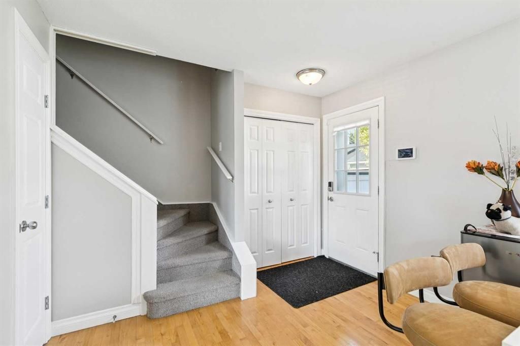 Bright entryway with white doors, staircase, gray carpet, and a tan chair by a window