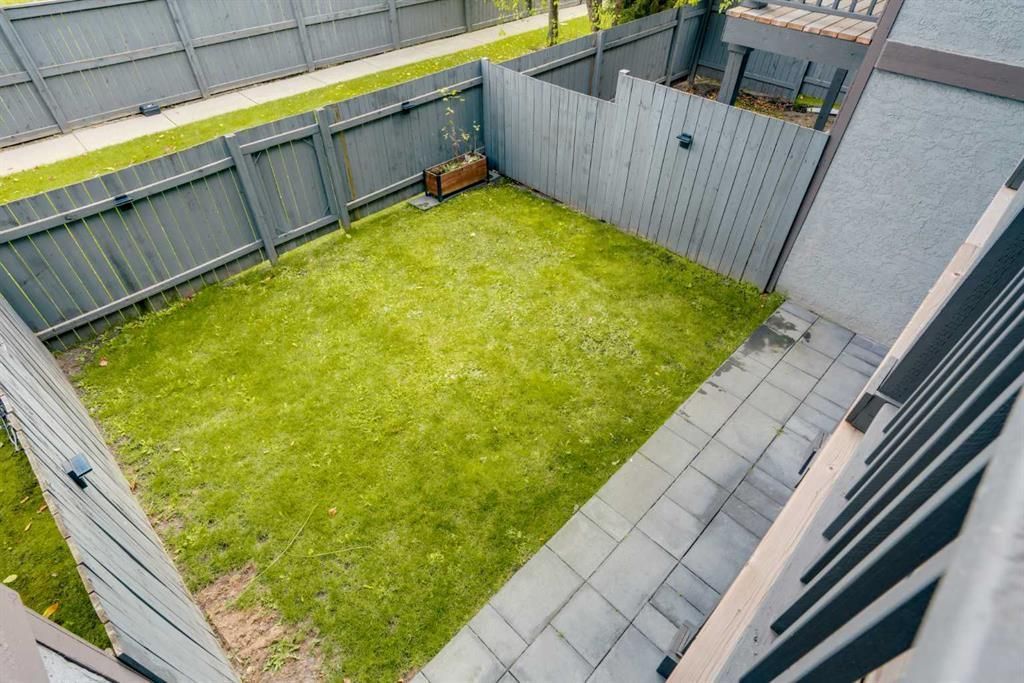 Small fenced backyard with green lawn, gray paving stones, and a wooden gate beside a white wall.