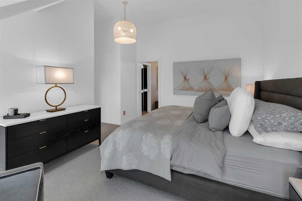 Modern bedroom with gray bedspread, black dresser, and soft pendant lighting