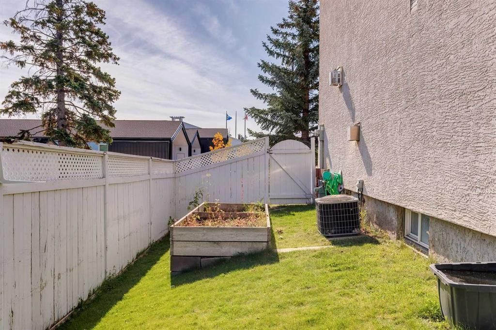 Small fenced backyard with grass, raised garden beds, a white fence, and a house wall on the right.