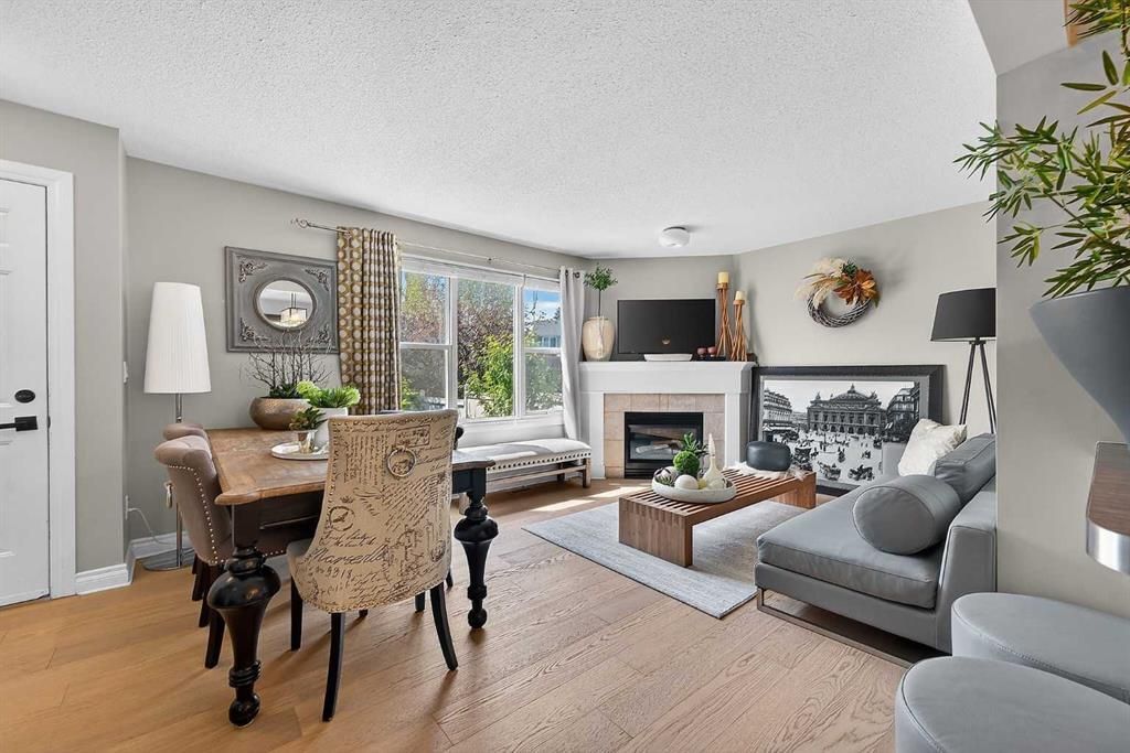 Bright living room with fireplace, gray sofa, dining table, and large windows with greenery outside
