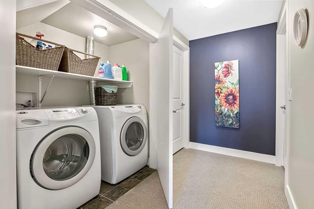Laundry room with white washer and dryer, shelves, and open door to a hallway with a blue accent wall and floral art