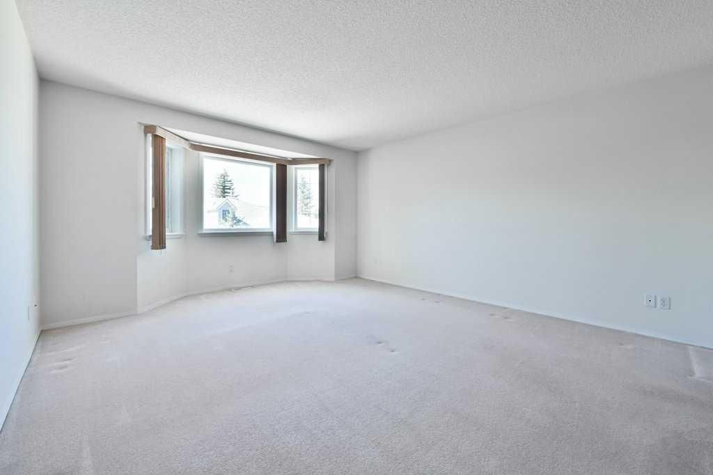 Empty white bedroom with carpet and a bay window letting in daylight
