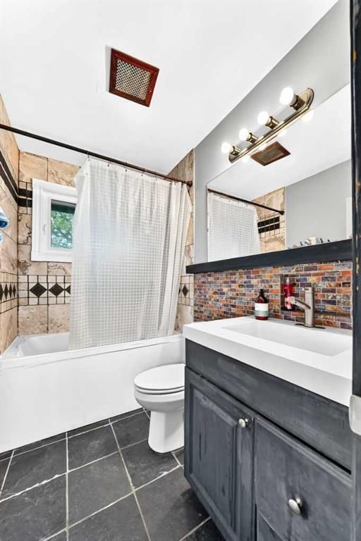 Small bathroom with dark vanity, white tub, tiled floor, and mosaic backsplash beside a shower curtain.