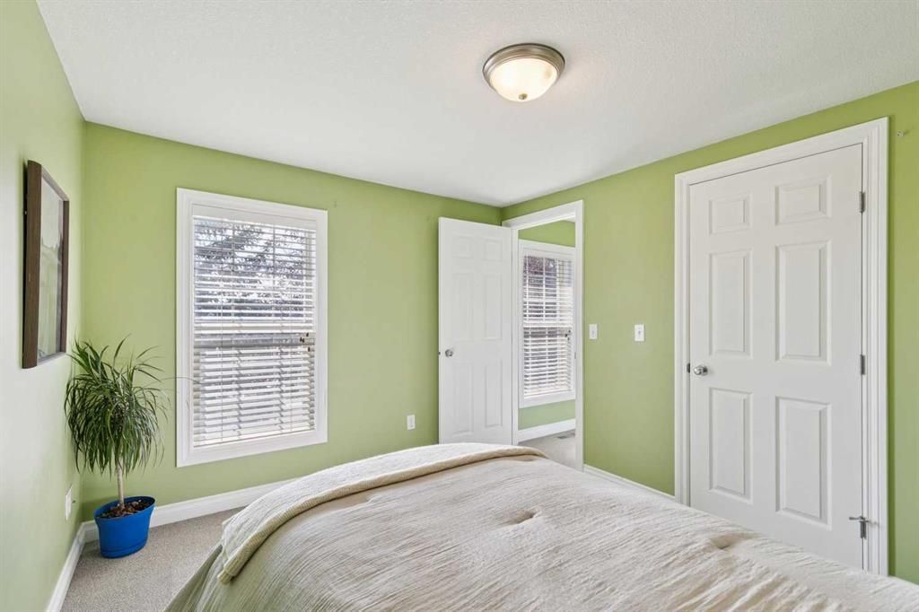 Bright green bedroom with white trim, bed, two windows, open closet, and potted plant.