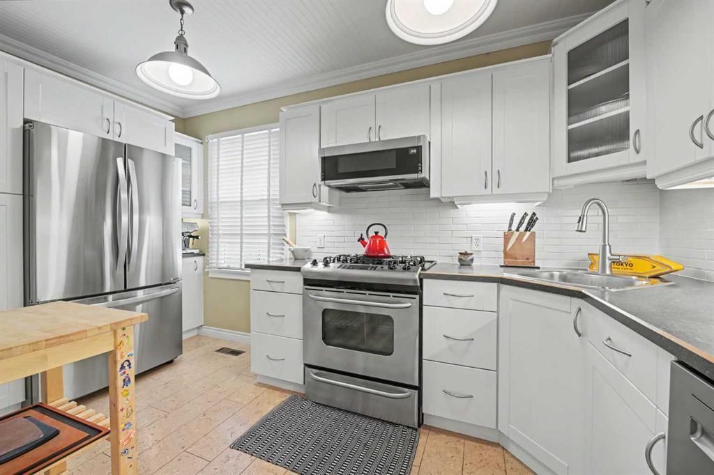 Bright white kitchen with stainless steel appliances, gray countertops, and a small island.