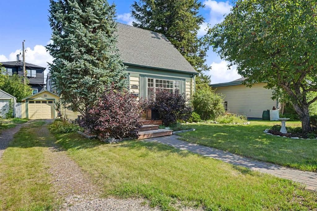 Small house with green roof, front yard, gravel driveway, and trees in bright sunlight