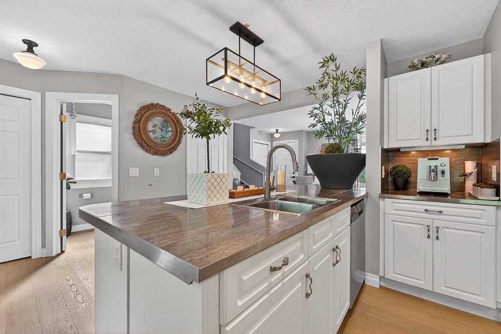 Bright modern kitchen with white cabinets, marble island, pendant lights, and potted plants