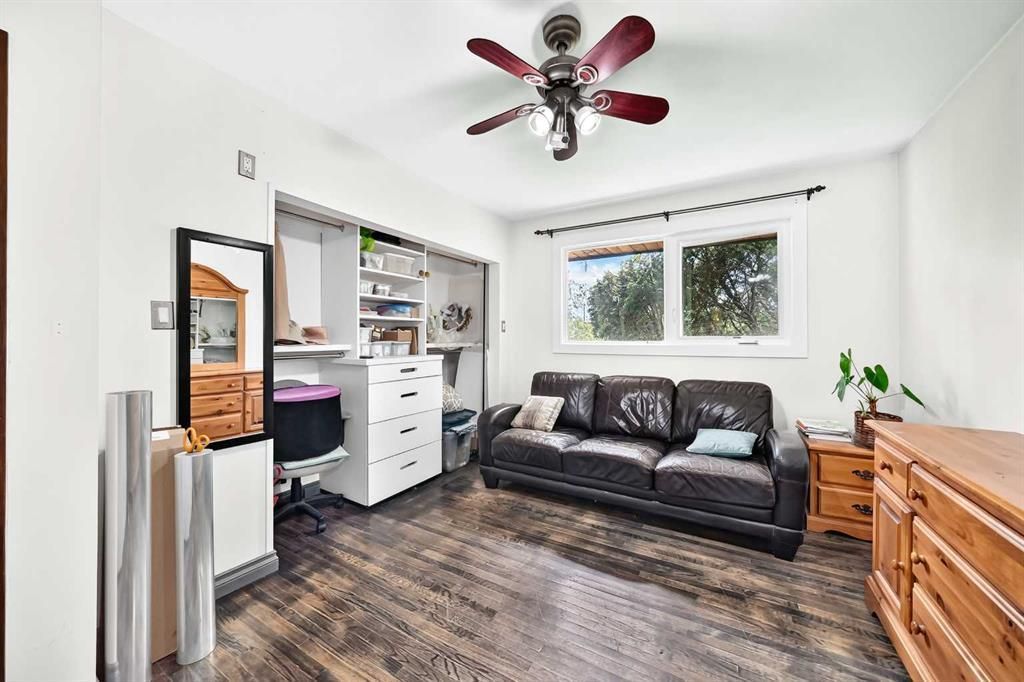 Bright bedroom with black bed, white dresser, ceiling fan, window, and wooden chest of drawers