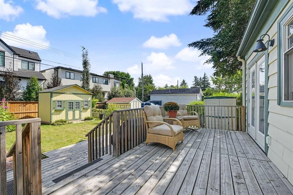 Wooden deck with wicker chairs outside a house, overlooking a fenced yard and neighboring homes under a blue sky