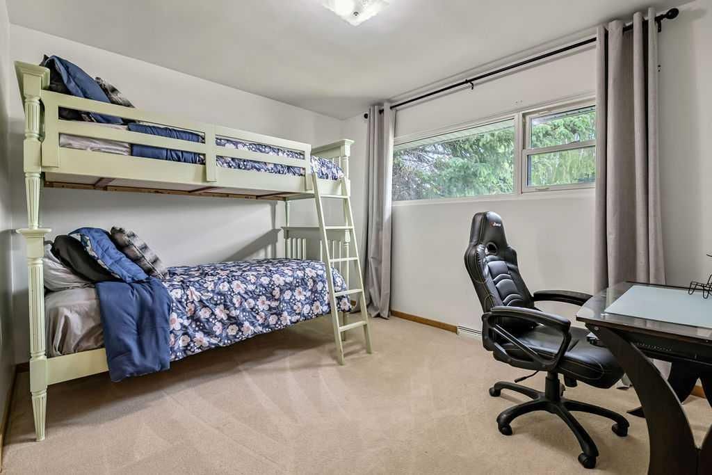Small bedroom with bunk beds, desk, office chair, and large window with blinds