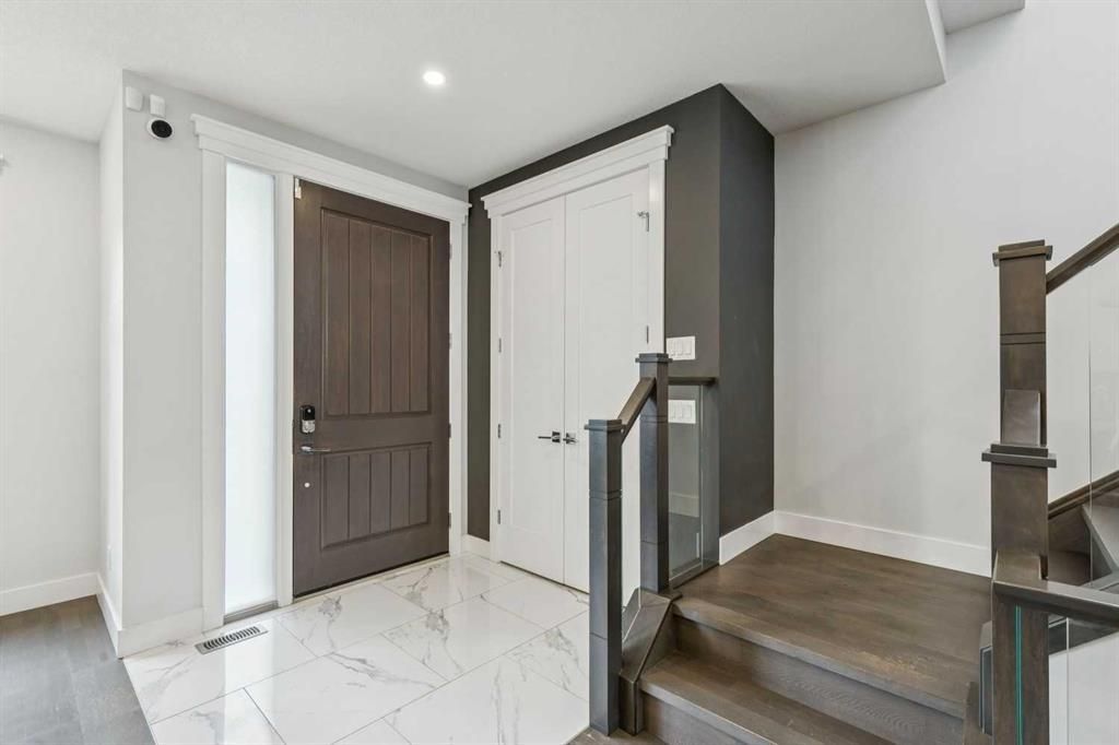 Bright entryway with white tile floor, dark wood door, white closet, and staircase railing.