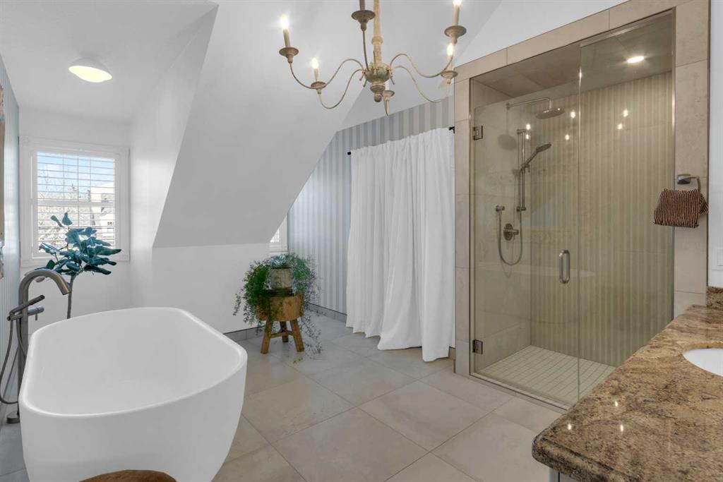 Bright white bathroom with a freestanding tub, glass shower, chandelier, and large window