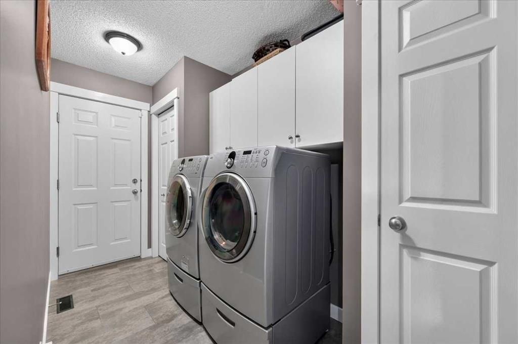 Laundry room with stacked washer and dryer, white cabinets, and gray tile flooring