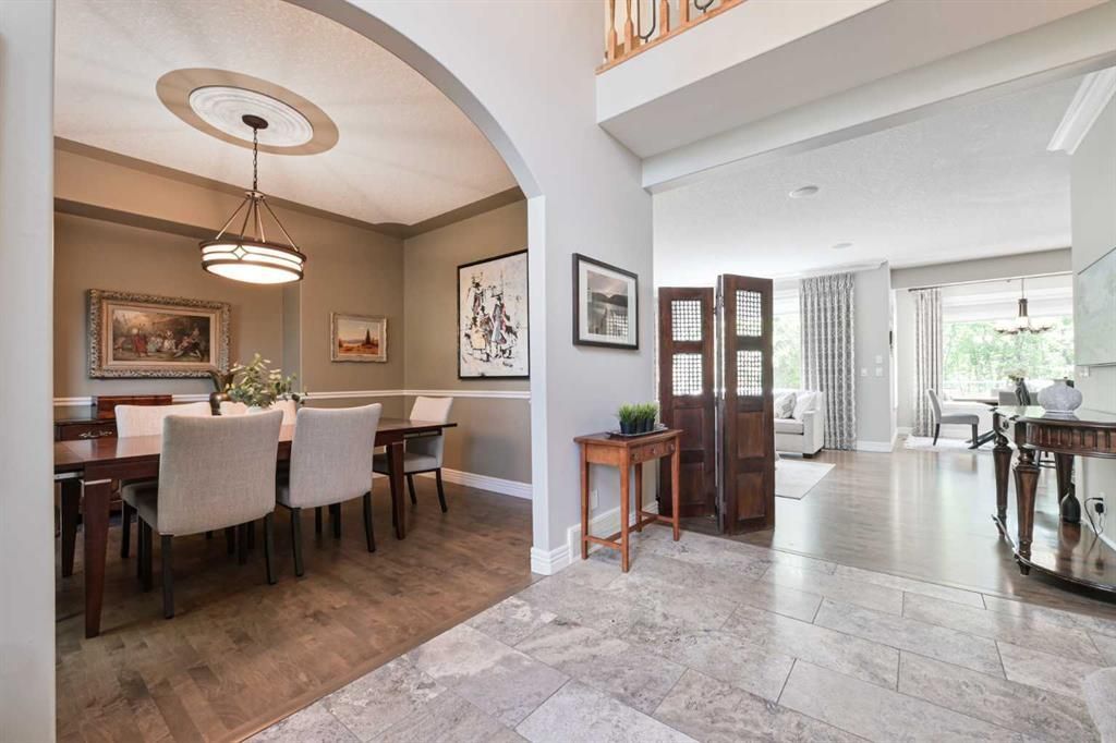 Bright dining room and foyer with white chairs, chandelier, tiled floors, and living area beyond