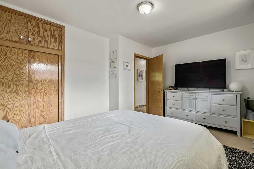 Bedroom with white bed, wooden closet, open door, and TV on a white dresser.