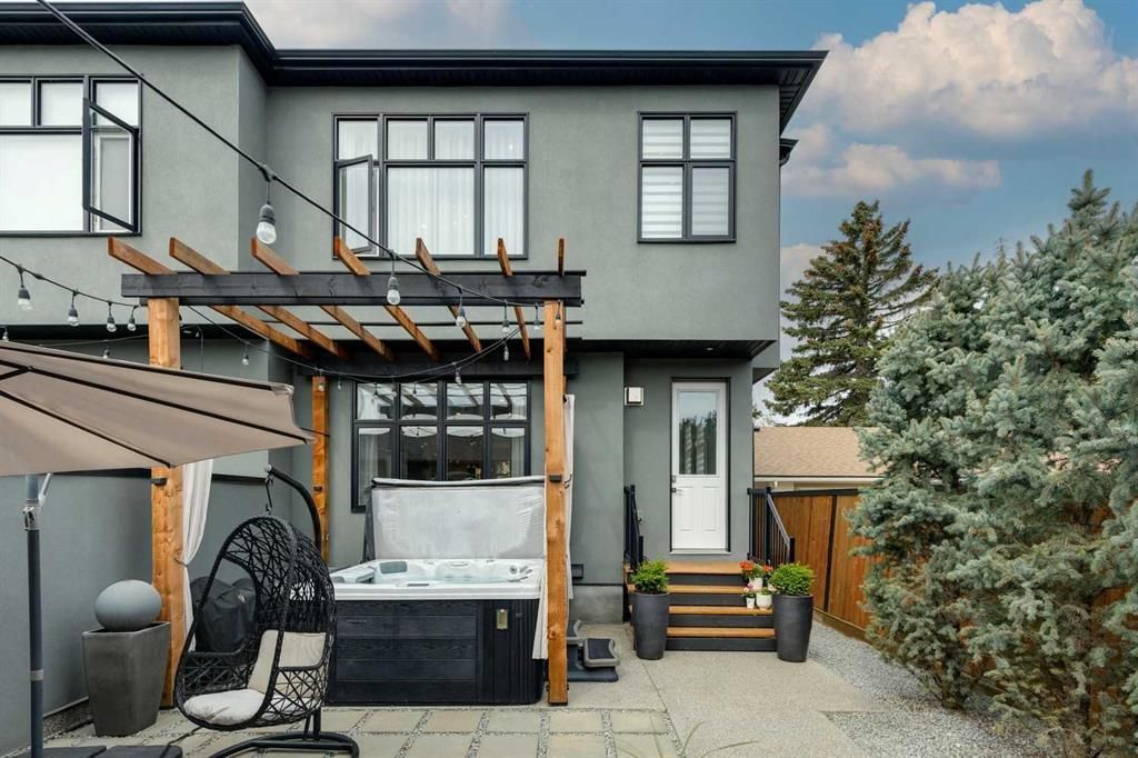 Modern gray two-story house with a covered patio, hot tub, and outdoor seating in a paved backyard