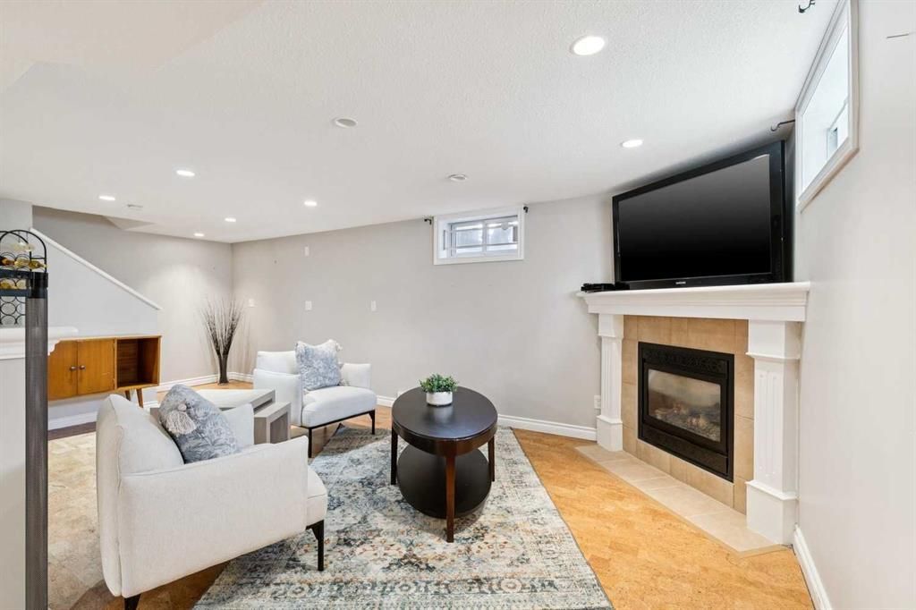 Bright living room with white sofas, patterned rug, fireplace, and wall-mounted TV.