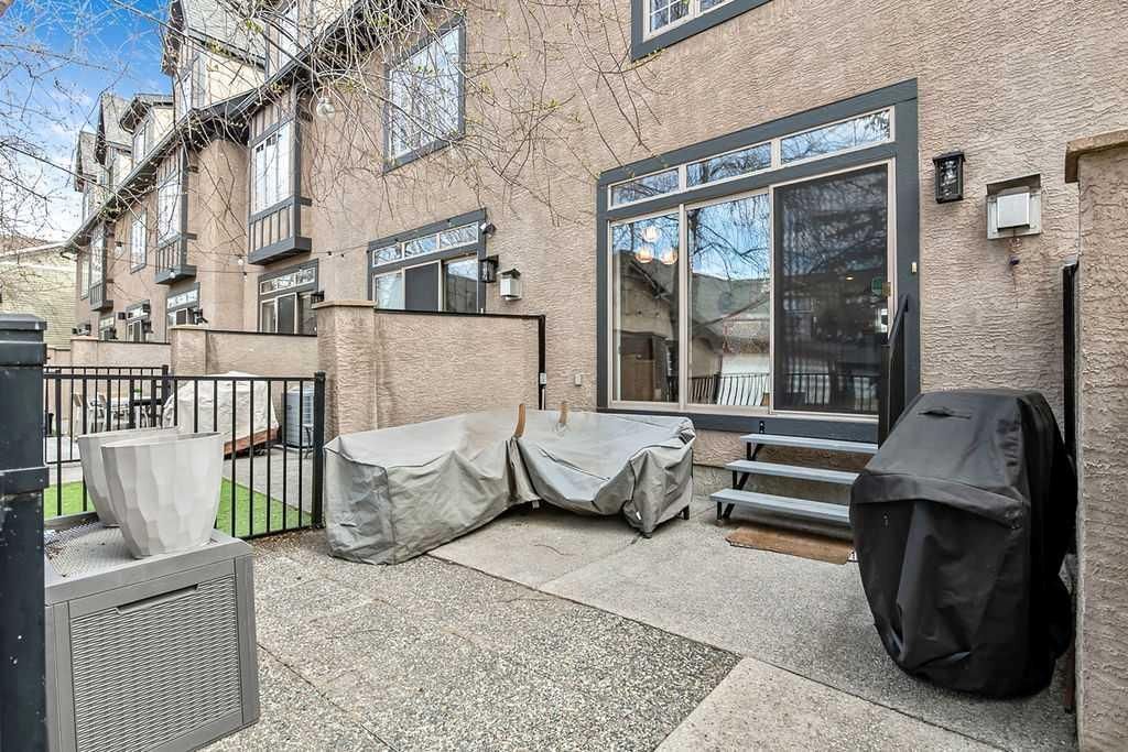 Backyard patio with covered furniture, grill, and large windows on a brick townhouse.