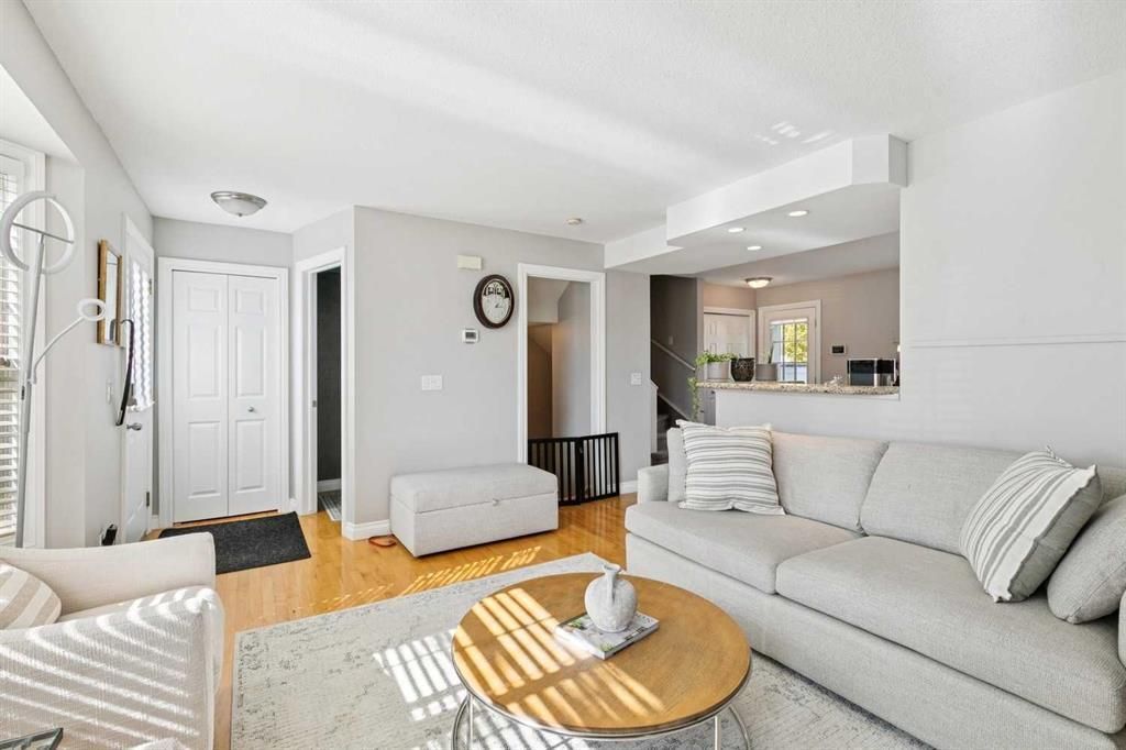 Bright living room with white sofa, round wood coffee table, and open kitchen in the background