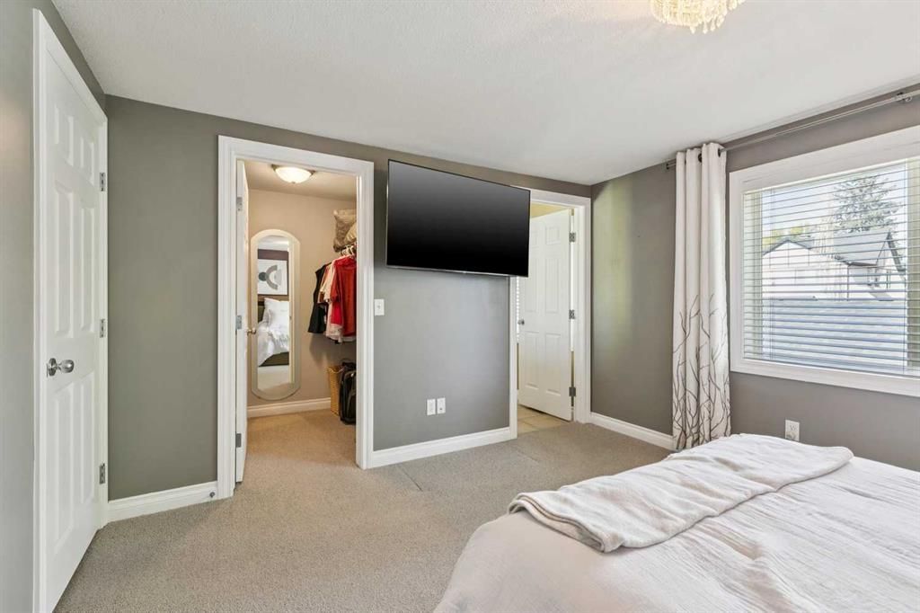 Bright bedroom with gray walls, a wall-mounted TV, open closet, and large window.