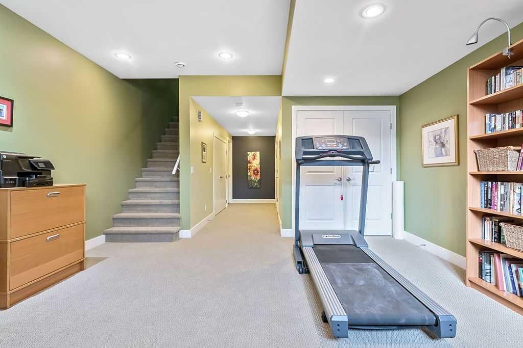 Basement rec room with treadmill, staircase, beige carpet, green walls, and bookshelves
