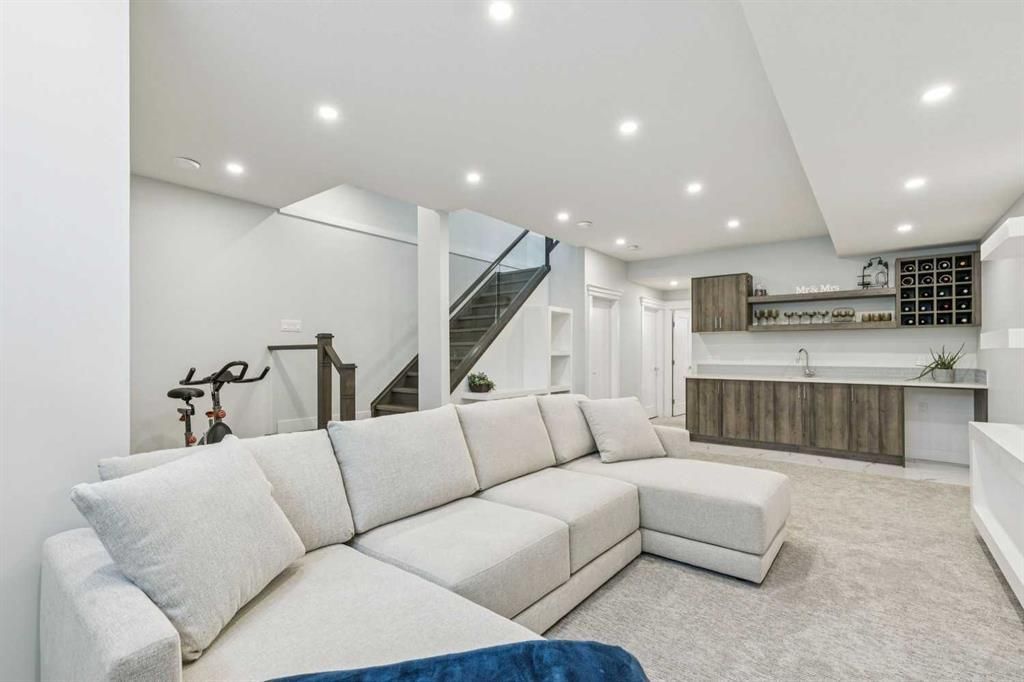 Bright modern basement lounge with sectional sofa, staircase, and built-in bar area
