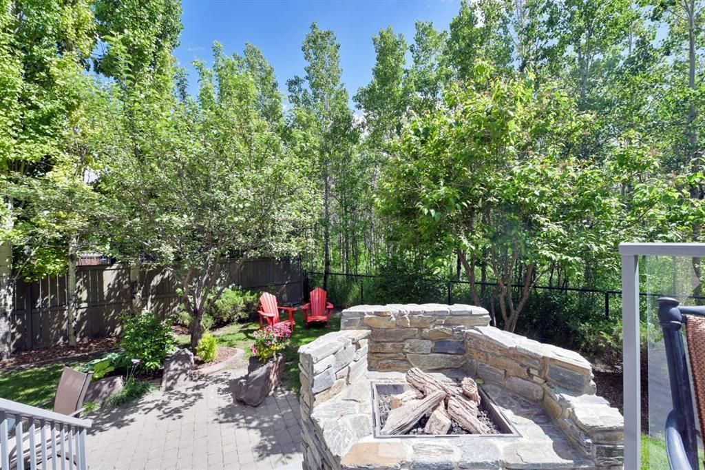 Backyard patio with stone fire pit, red chairs, and tall green trees in bright sunlight