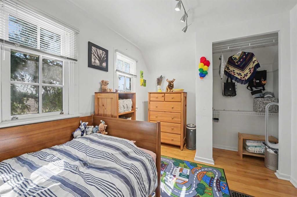 Bright bedroom with twin bed, wooden dresser, closet, and colorful wall art under a window.