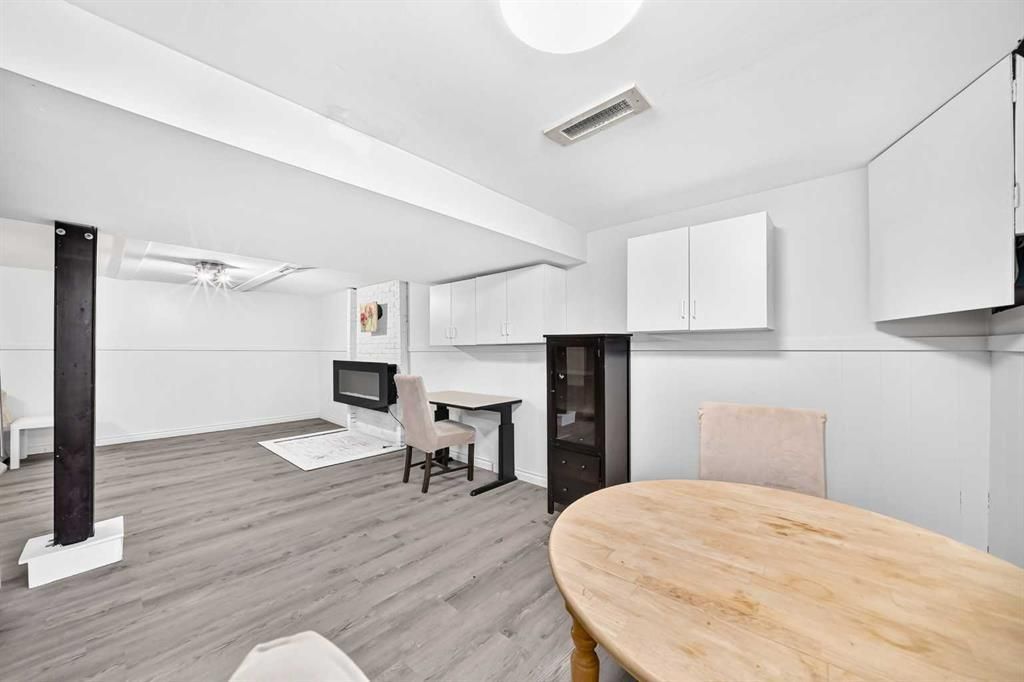 Bright modern living room with gray flooring, white cabinets, a round wooden table, and a small desk area