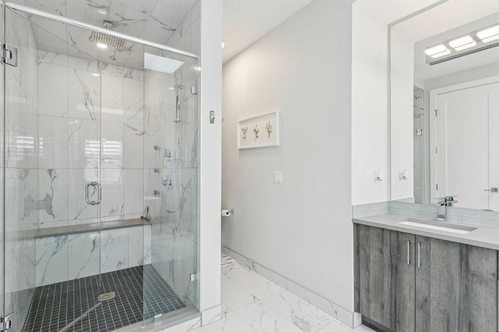 Bright modern bathroom with glass shower, marble tile, and vanity sink with large mirror