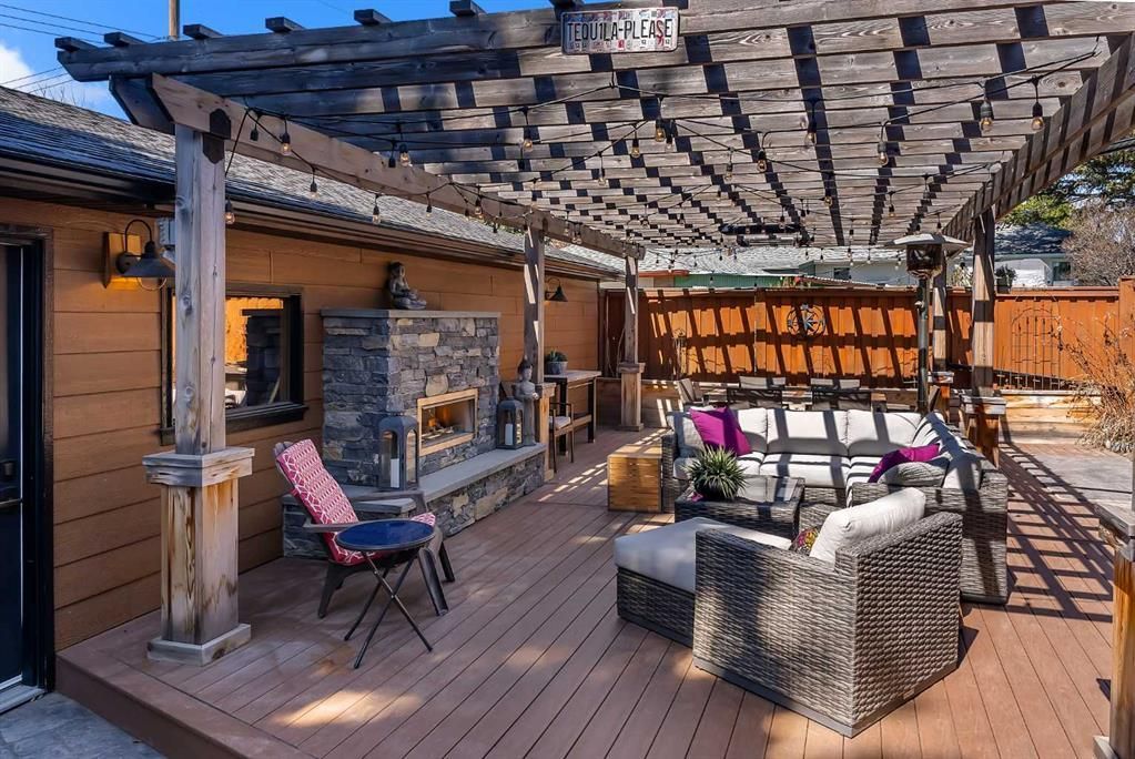 Patio seating area with wicker chairs, pergola shade, and a stone fireplace in warm sunlight