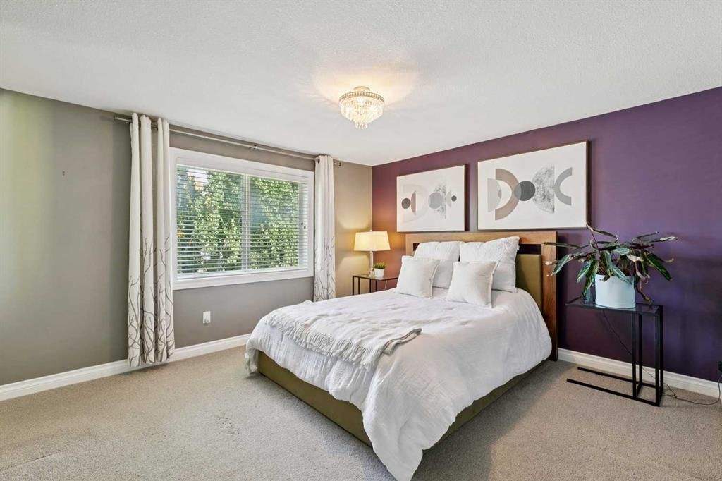 Bright bedroom with a white bed, purple accent wall, window, and bedside lamp