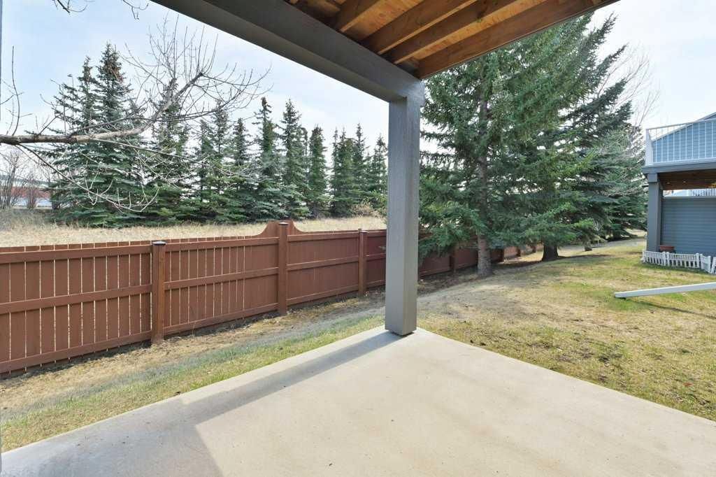 Covered backyard patio with concrete floor, wooden fence, and evergreen trees in a suburban yard.