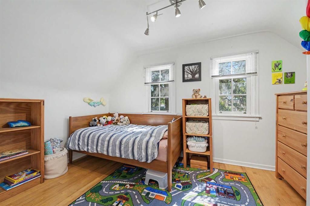 Bright child’s bedroom with twin windows, wooden bed, shelves, dresser, and colorful rug.