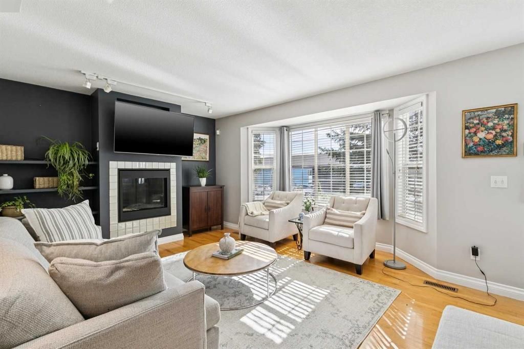 Bright living room with fireplace, two armchairs by tall windows, and sectional seating on a rug.