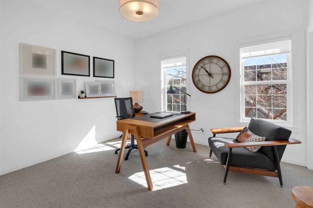 Bright home office with wooden desk, leather chair, wall clock, and two windows letting in sunlight