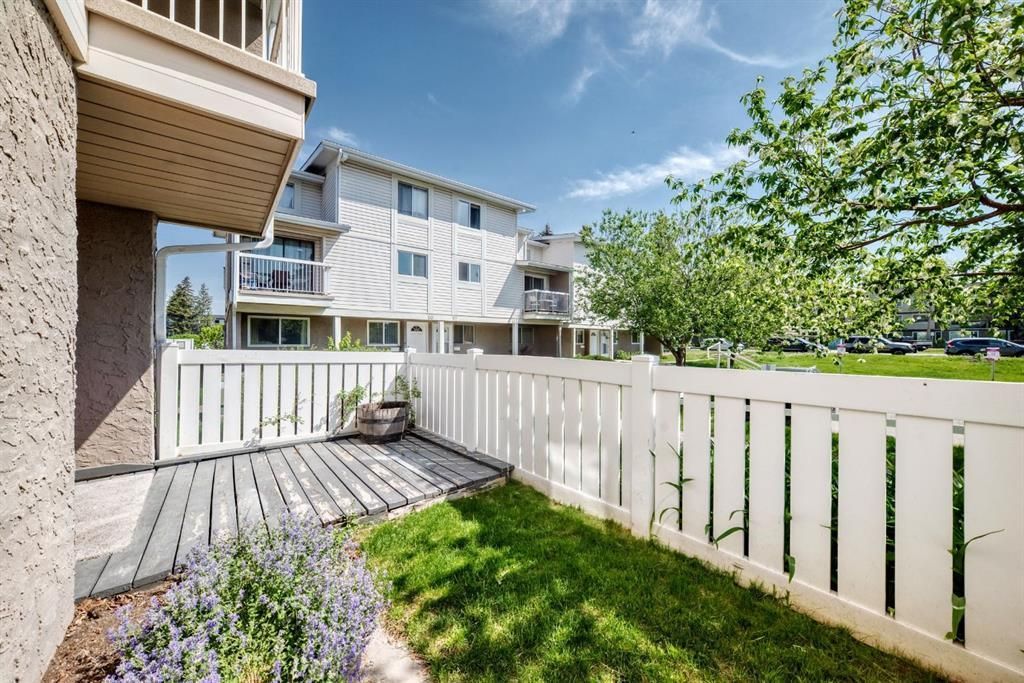 Patio with white fence, grass, and apartment buildings on a sunny day