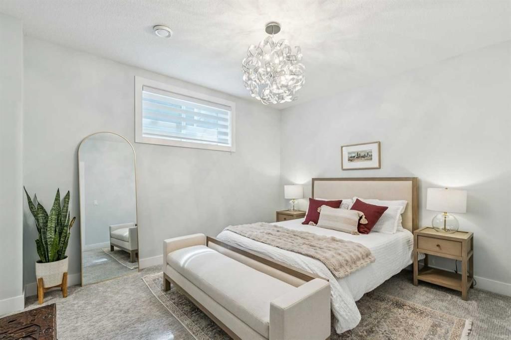 Bright white bedroom with a bed, chandelier, mirror, bedside table, and potted plant